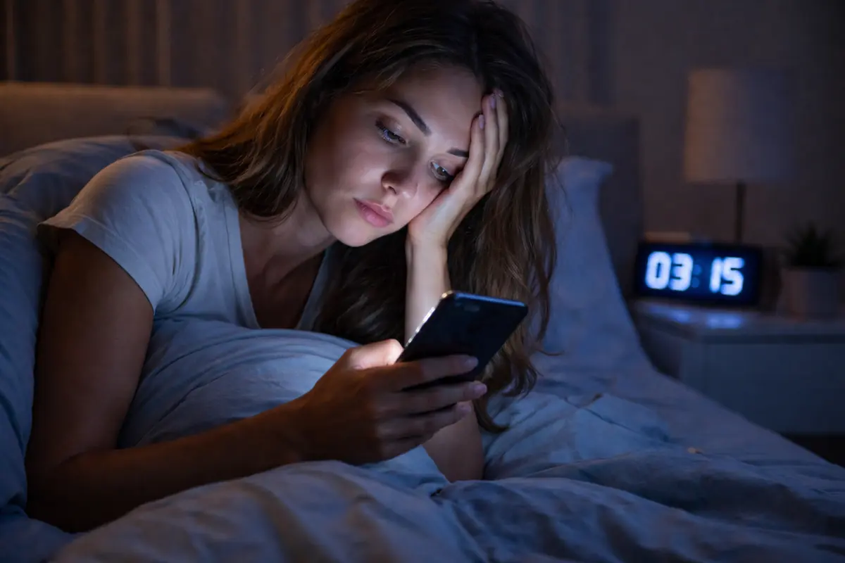 Donna sveglia di notte guarda lo smartphone durante la Giornata Mondiale del Sonno, simbolo dei disturbi del riposo e dell’insonnia